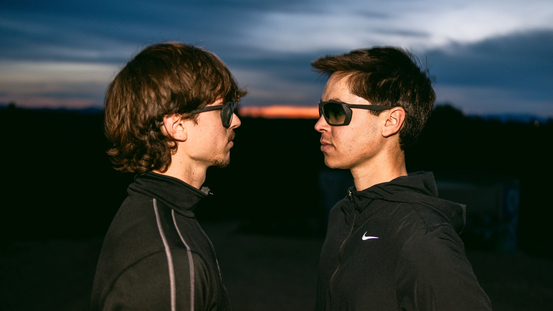 Two men looking at each other while the sun sets in the background.